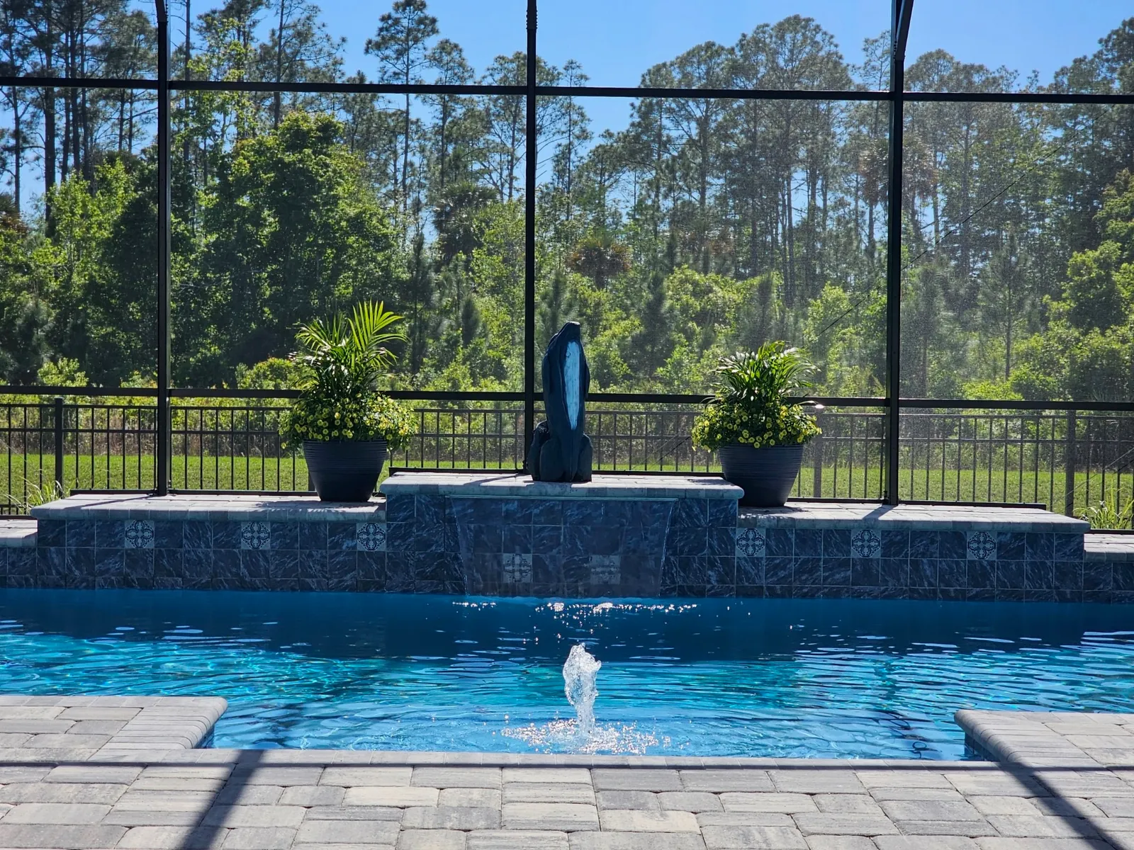 Raised marble-tile wall water feature with sculpture and spillover into the pool