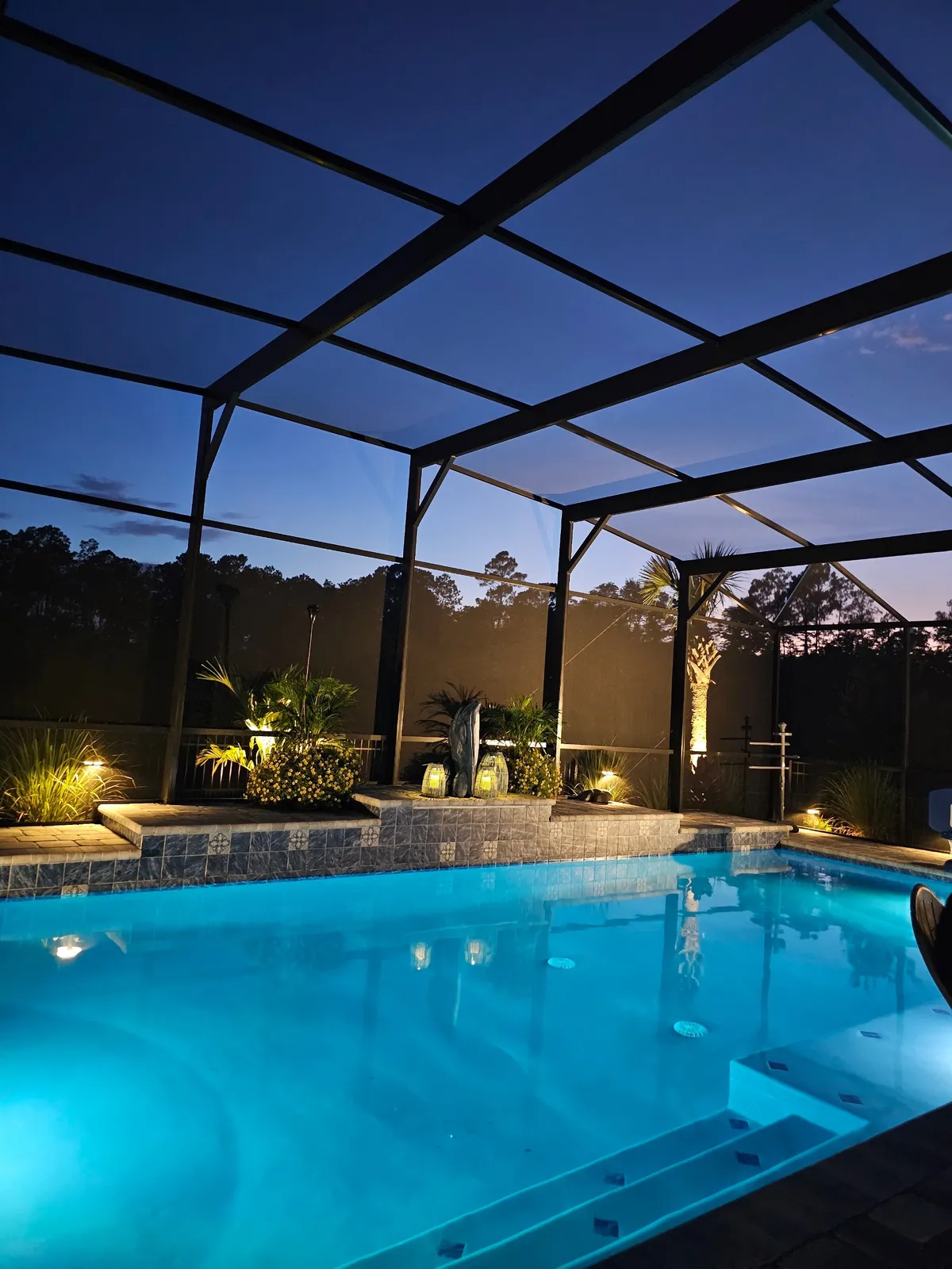 Screen-enclosed pool glowing with LED lighting at dusk