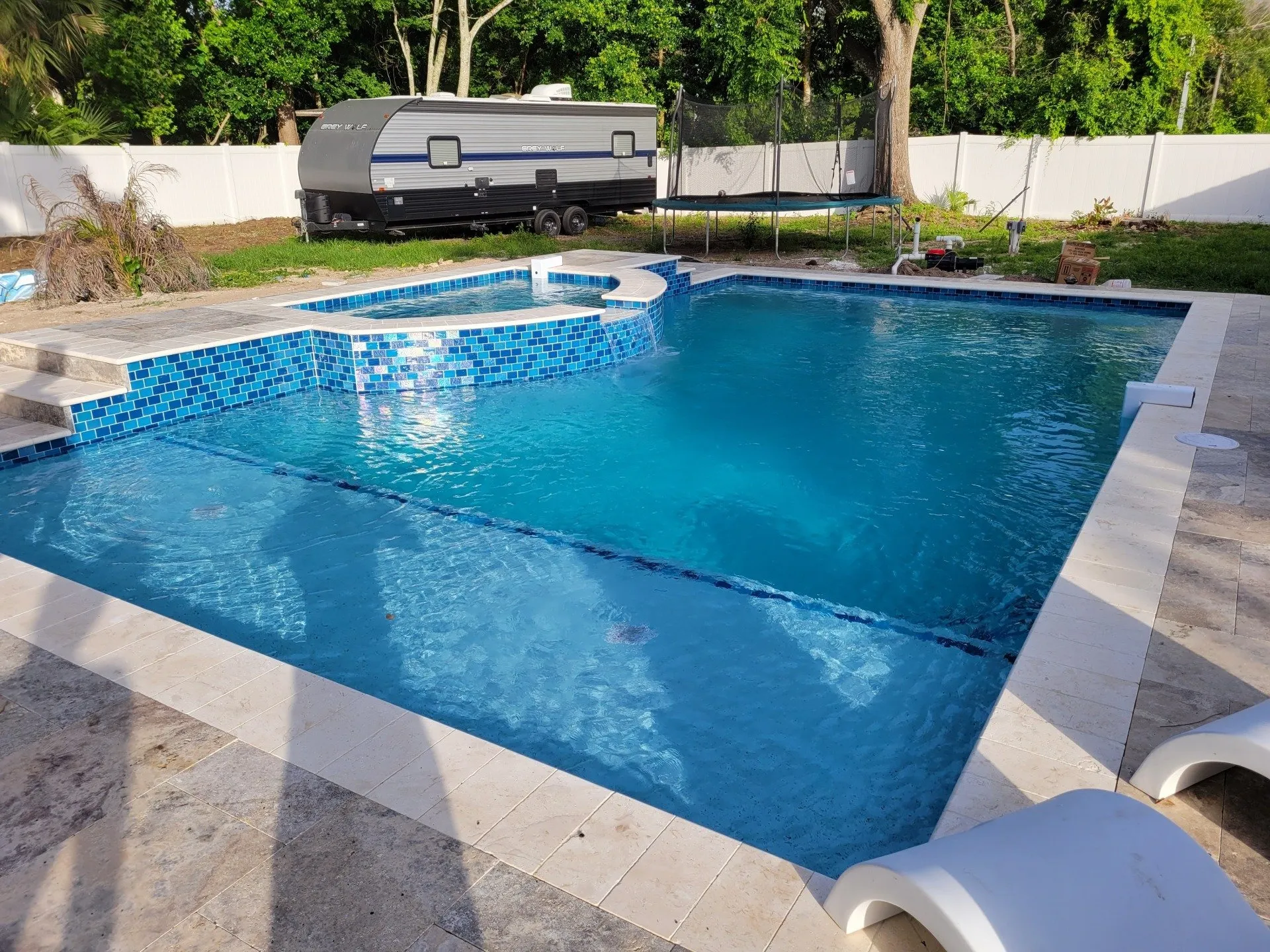 New construction pool and spa with blue glass tile and travertine deck