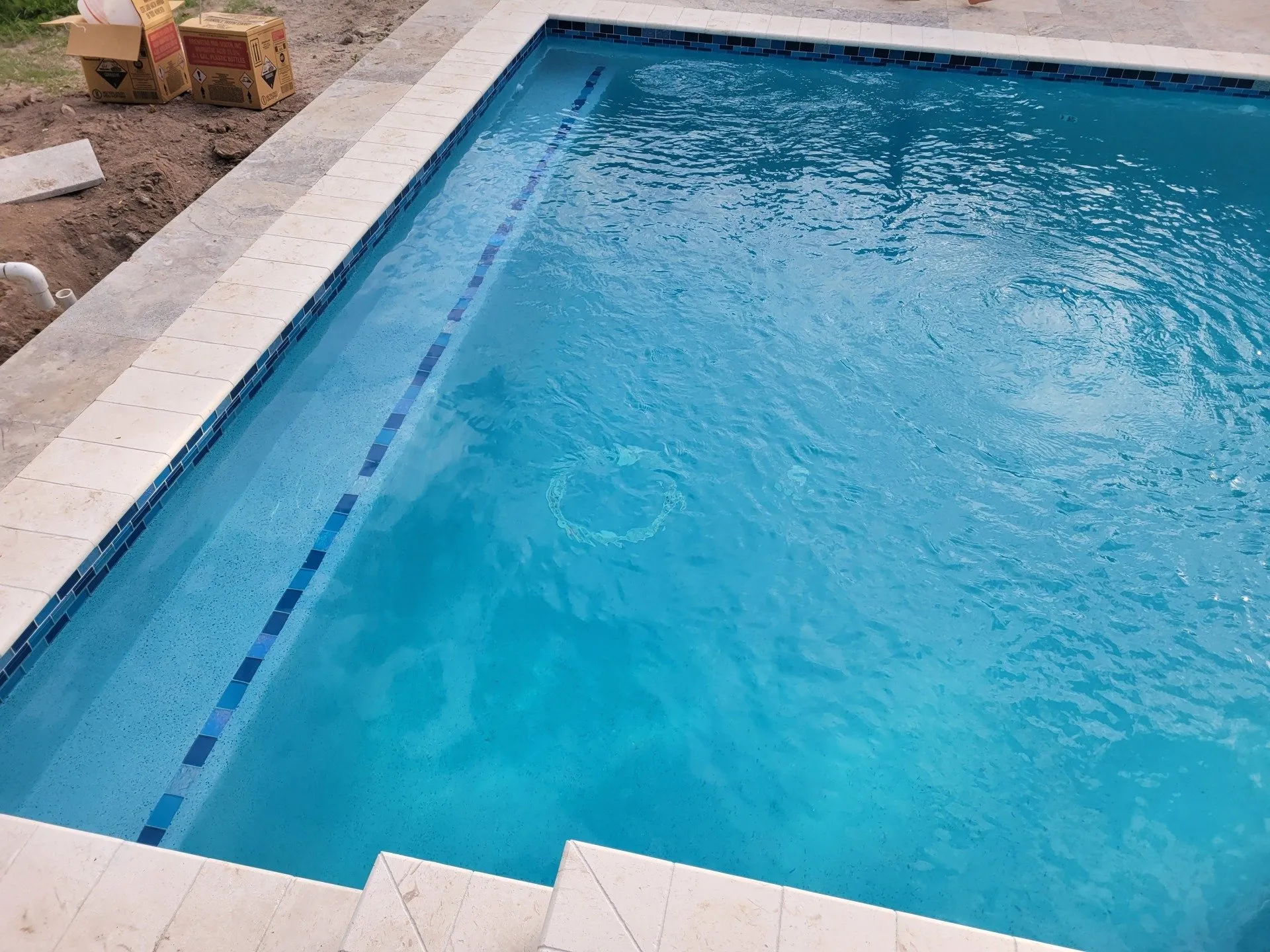 Close-up of blue glass waterline tile and travertine coping