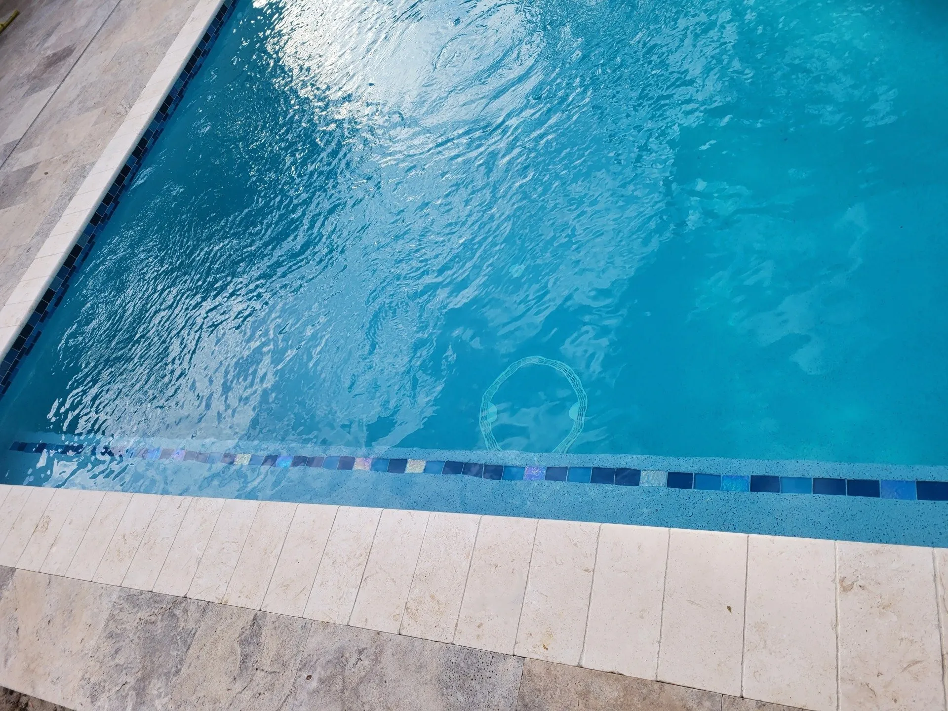 Detail of glass waterline tile with travertine coping