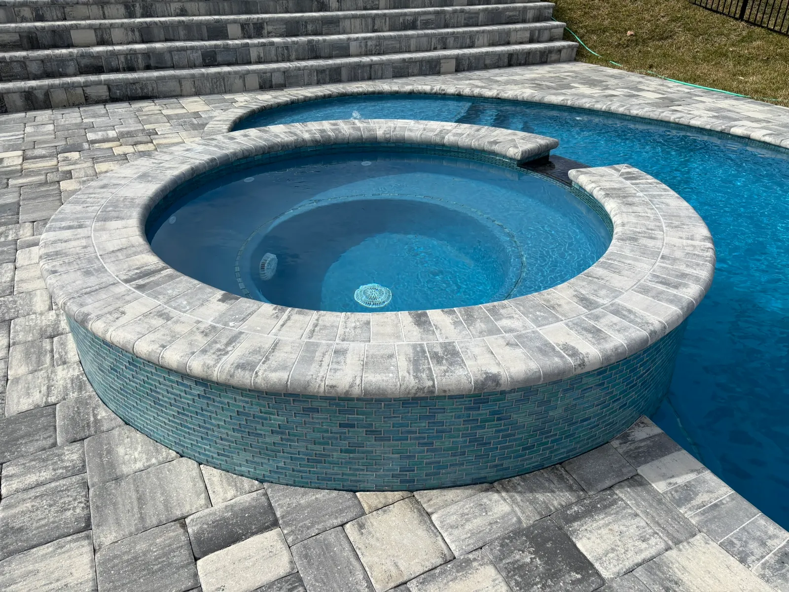Close-up of a round spa finished in blue glass tile with a spillover into the pool