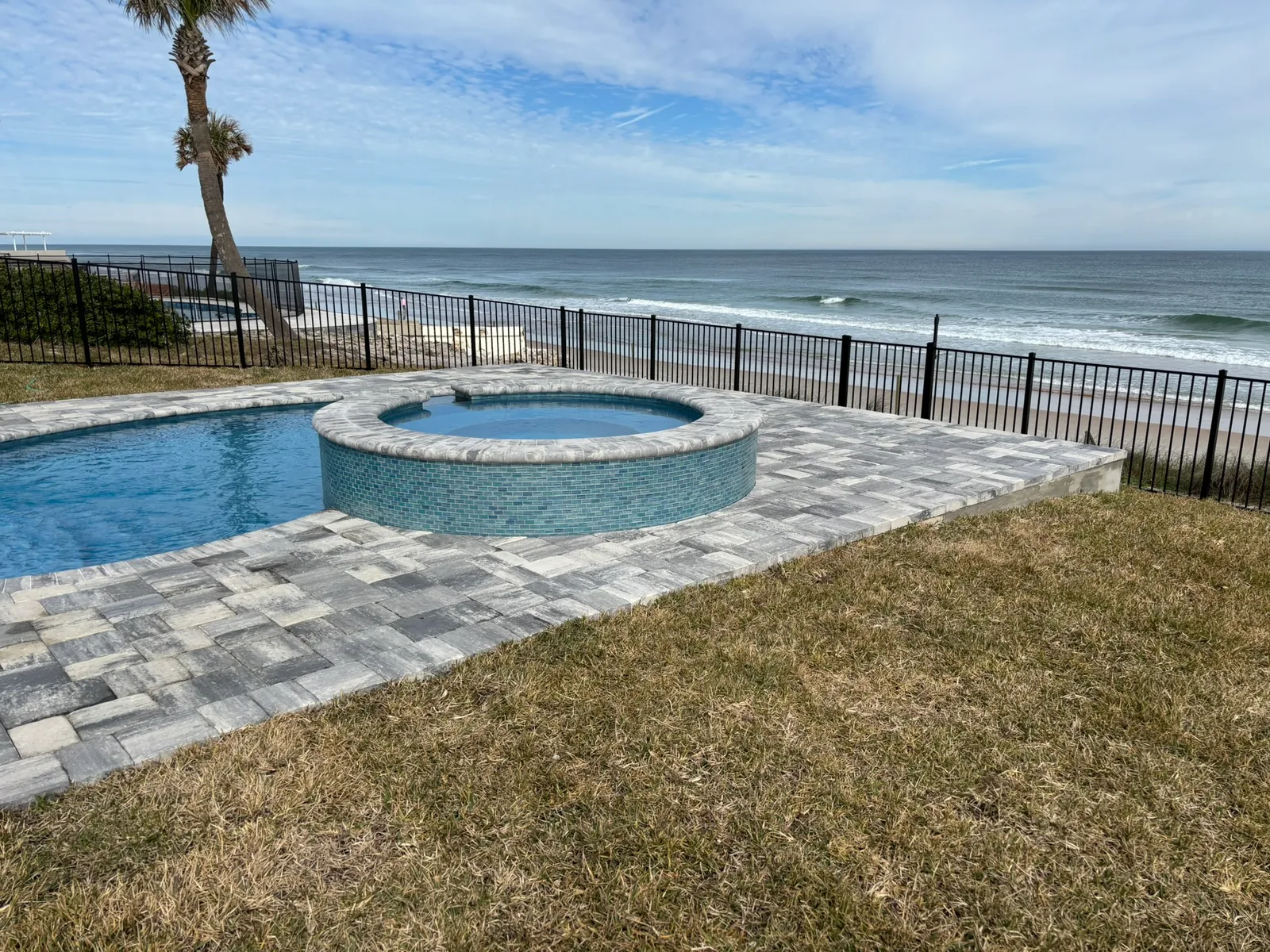 Beachfront pool and round spa with blue glass tile and travertine coping