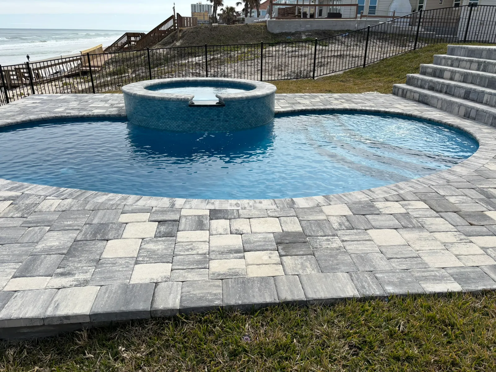 Freeform pool with raised spillover spa on a paver deck steps from the ocean